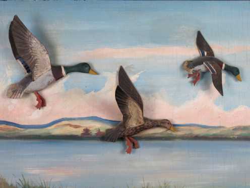 Three carved and painted mallards in flight set on panel depicting a pond with mountains